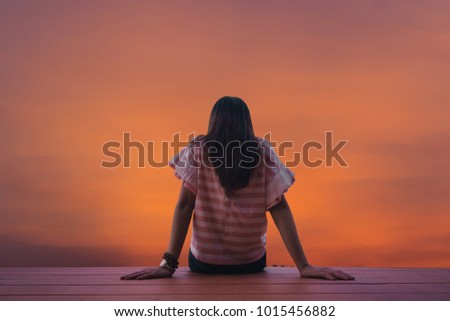 The silhouette, the back of the girl sitting on the balcony in the morning alone to wait for her lover back.
Solar backgrounds are rising up the horizon in the beautiful summer morning.