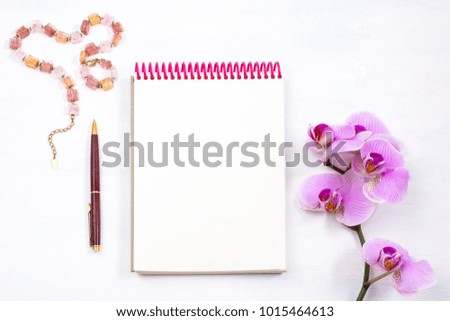 Female workspace mockup with notepad, pen and pink orchid on white background, top view
