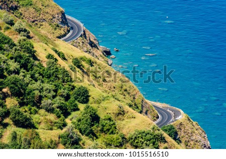 Aerial view of the SS113, a winding road on the edge of a rocky cliff above the deep blue Tyrrhenian sea between Capo Skino and Capo Calava on the northern coast of Sicily.