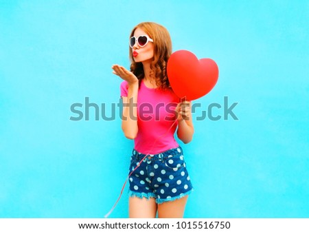 Pretty woman sends an air kiss holds red balloon in the shape of heart on a blue background