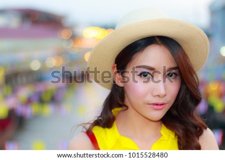 Close up portrait young asian beautiful girl with long hair wearing a hat and a yellow shirt  at night  floating market in Amphawa, Thailand,Bokeh background