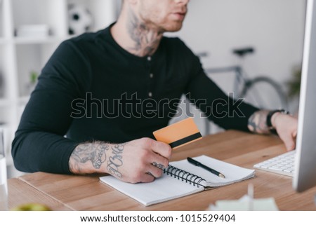 cropped shot of young businessman holding credit card and using desktop computer