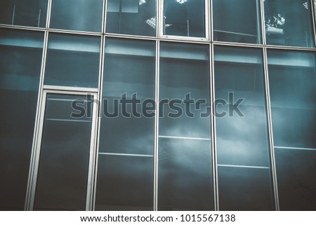Business glass office in town work deals city  . Blue tinted photo of hi-tech modern stylish avant garde windows and workers . Background symetric texture pattern photo from down. 