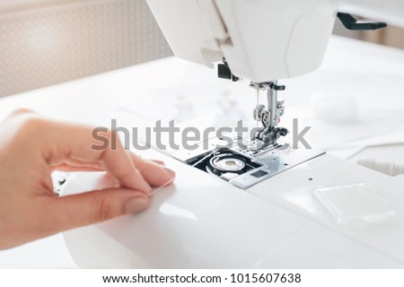Young seamstress adjusts the sewing machine to work. Hands closeup. Selective focus. Toning.