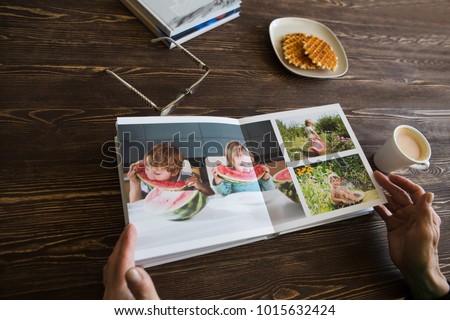 the Hand senior woman holding a family photo album against the background of the a wooden table.
