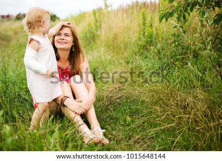 Mother and child girl playing, kissing and hugging in green field. Happy mother's day. Spring family holiday concept. Outdoor portrait