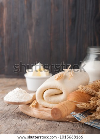 Puff pastry dough. Homemade folded raw puff pastry on a wooden cutting board on a rustic wooden surface (table). Making puff pastry. Dough's rolls with a rolling pin, flour, butter, wheat spikelets. Royalty-Free Stock Photo #1015668166