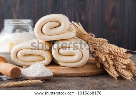 Puff pastry dough. Homemade folded raw puff pastry on a wooden cutting board on a rustic wooden surface (table). Making puff pastry. Dough's rolls with a rolling pin, flour, butter, wheat spikelets. Royalty-Free Stock Photo #1015668178