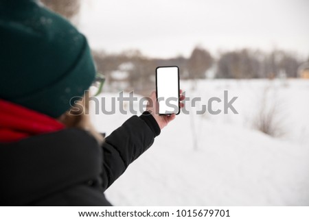 A girl in a black, winter jacket, taking photos of winter dervishes. Holds the phone with your left hand.