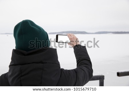 The girl is making a photo on the phone in the cold winter. Holds the phone with your right hand.