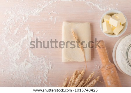 Puff pastry dough. Homemade folded raw puff pastry on a table. Making puff pastry. Dough's roll with a rolling pin, flour, butter, wheat spikelets with copy space. Royalty-Free Stock Photo #1015748425