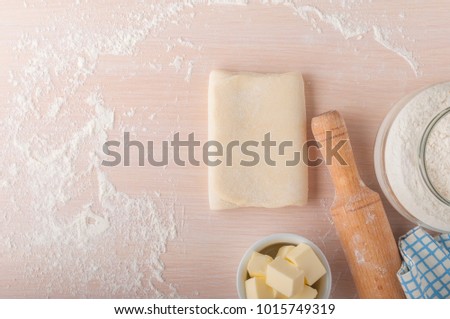 Puff pastry dough. Homemade folded raw puff pastry on a table. Making puff pastry. Dough's roll with a rolling pin, flour,  butter and cloth with copy space. Royalty-Free Stock Photo #1015749319