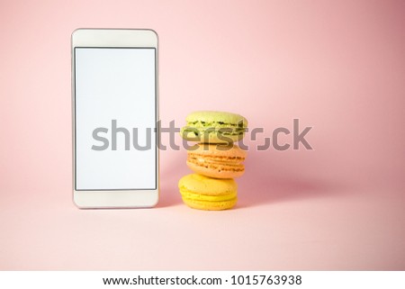 Stacked colorful macarons and smartphone with blank screen on the pink background.  