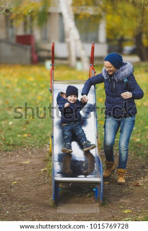 Young woman walk in green yellow fall autumn park with little cute child baby boy on nature. Mother, kid son fun rest, ride children s slides on playground. Family day 15 of may, love parents concept