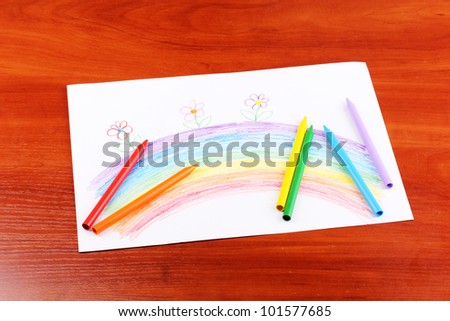 Children's drawing of rainbow and pencils on wooden background
