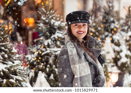 Portrait of pretty young woman wears stylish black hat before Christmas city background in snow time