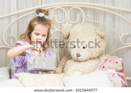  Lovely little girl in violet dress playing with toys on a white airy bed