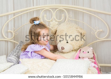 Lovely little girl in violet dress playing with toys on a white airy bed
