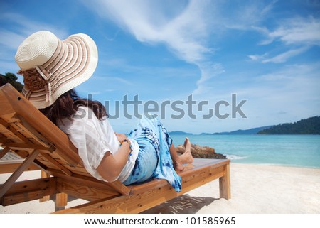 Young woman enjoying the sea view sitting on a beach's chair close to the sea