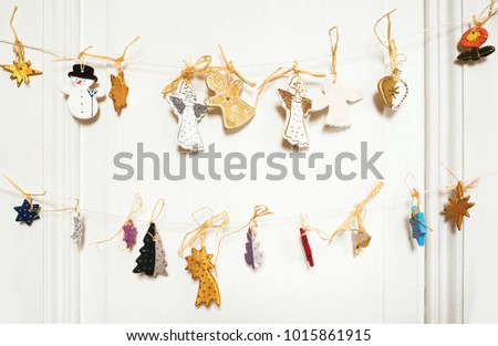Colorful tiny christmas decorative bauble (angel,snowman,star,apple,flower) hanging on string on white wall.