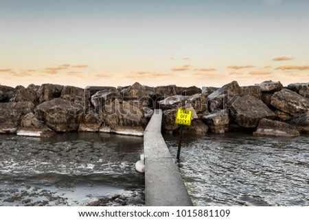 Metal post leading to rock pile on lake with yellow sunset