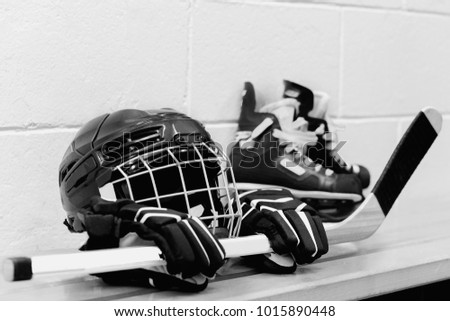 White and black photo of girl's hockey gear: helmet, gloves, sticks, skates with laces