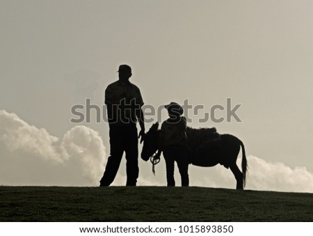Donkey with short and tall man silhouetted against a natural horizon with clouds. There are several stories which could start or end with this picture  which is a real photograph of a casual moment
