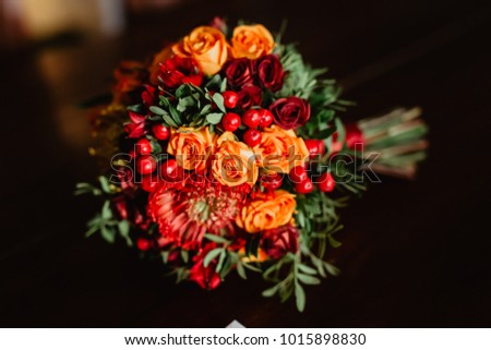 Wedding red, yellow and orange bouquet of roses and peonies on the table close-up. The bride's bouquet. Bridal bouquet of flowers - ideal details for beautiful bride. Morning details.