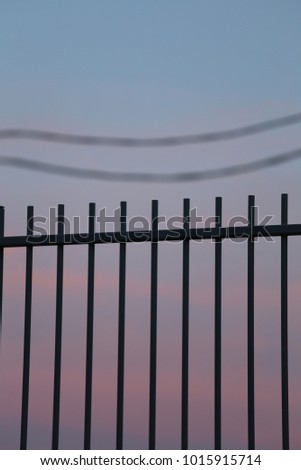 Close up view of part of a metalic barrier and two electric cords in background. Purple and blue clear sky. Abstract urban picture with simple elements. Silhouettes created by the evening light.  
