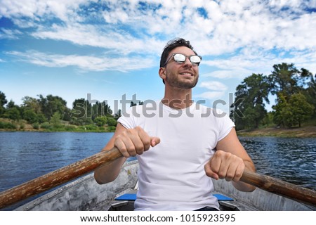 A handsome muscular bearded man in sun glasses and white t shirt is driving a boat on a river or lake. Beautiful happy 
guy swimming in a boat on a warm sunny day feeling free