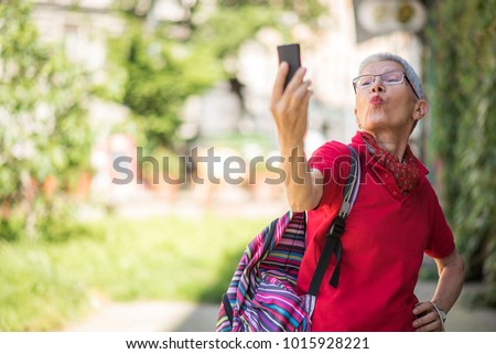Cheerful senior woman sending kisses to her family or friends over her cell phone, enjoying her summer trip