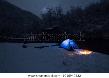Blue tent and bonfire. Beautiful dark wilderness in background. 
