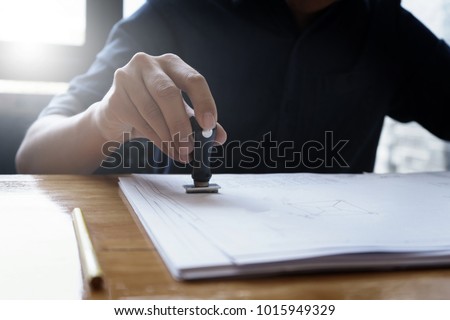 Architect or engineer stamping the document or blueprint on wooden desk - architectural project, Construction concept. Royalty-Free Stock Photo #1015949329