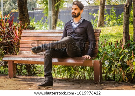 This picture shows a portrait of a man sitting on a bench at the park.