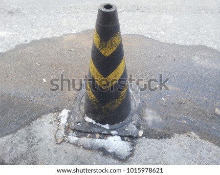 Traffic cone with yellow and grey strips on grey asphalt, Road construction warning cone