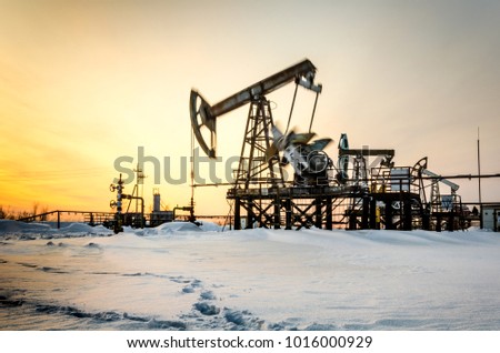 Pump jack, wellhead and pipeline during sunset in the oilfield. Winter period. Oil and gas concept. Toned. Motion blur.