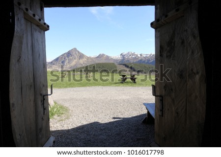 Opening ancient wooden doors in the shadow as in the foreground and a view of mountain, blue sky and green lawn as in the background