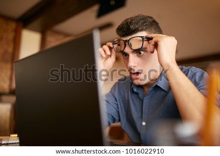Shocked freelancer hipster man looks to laptop screen and can not believe unpleasant news. Pop-eyed frightened businessman trader raises one's glasses above his eyes. Trader monitoring stock exchange Royalty-Free Stock Photo #1016022910