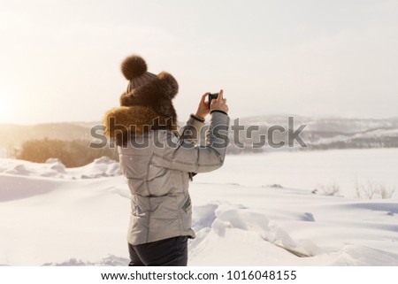 woman in winter suit photographing winter landscape