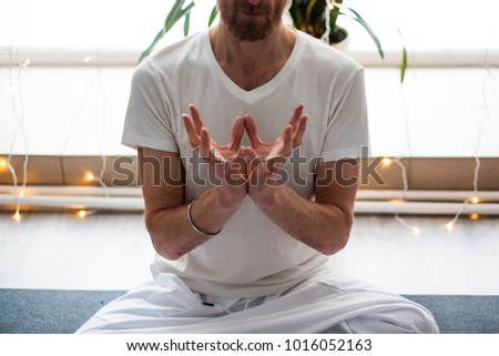 Kundalini yoga. Man holding mudra (special hands position) and wearing white clothes. Doing asana and mailtaining balance inside. 
