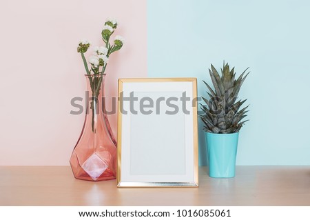 Modern home decor mock up with gold blank photo frame, vase and tropical plant on pink blue background.