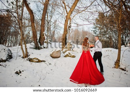Amazing couple in winter fairytale forest in love. Girl in red beautiful dress. Valentine's Day theme.