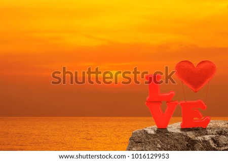 Red love alphabet and fabric heart ballon on rock over sunset sky and sea, Valentines day concept