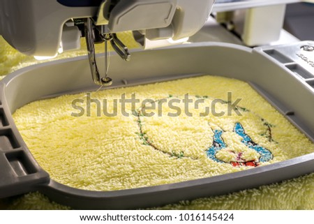 Close up image of workspace embroidery machine embroidering cartoon rabbit on yellow towel