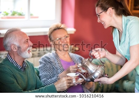 Young beautiful smiling careful nurse serves tea for patients at nursing home