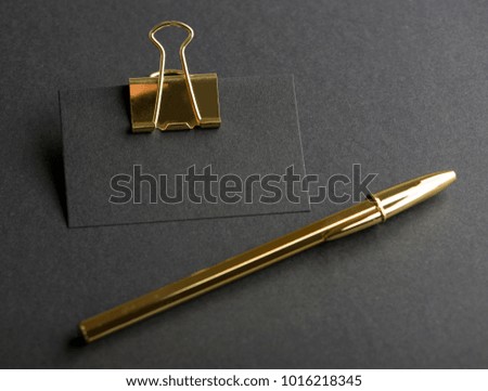 Black business card with golden clothespin next to golden  pen on black background. Mockup.