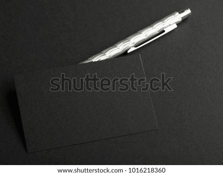 Black business card next to gray pen on black background. Mockup.