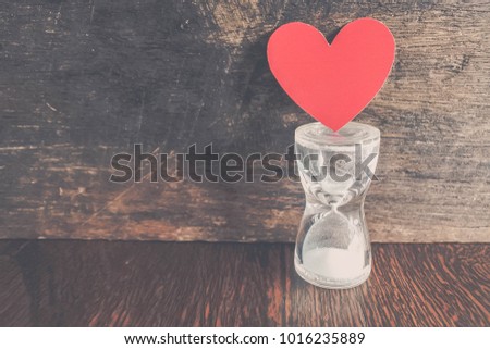 red heart paper placed on a sandglass with wooden background. The happiness and love surrounds human beings as well. Vintage style photo.