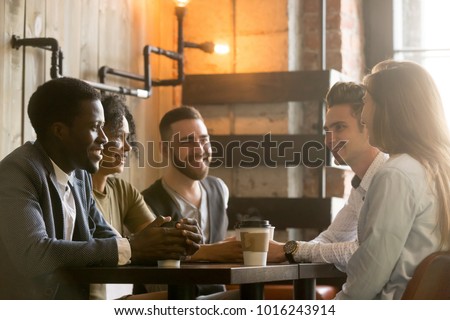 Multiracial happy friends talking and drinking coffee sharing coffeehouse table, diverse african and caucasian millennial young people smiling enjoying pleasant conversation in cafe at coffee break Royalty-Free Stock Photo #1016243914