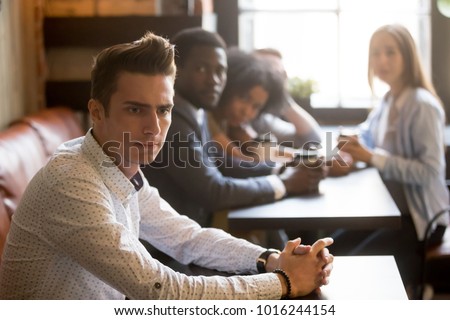 Diverse people looking at thoughtful frustrated man in cafe, sad misunderstood guy feels offended ignoring multiracial friends sitting alone at table, excluded outstand person suffers from bullying Royalty-Free Stock Photo #1016244154